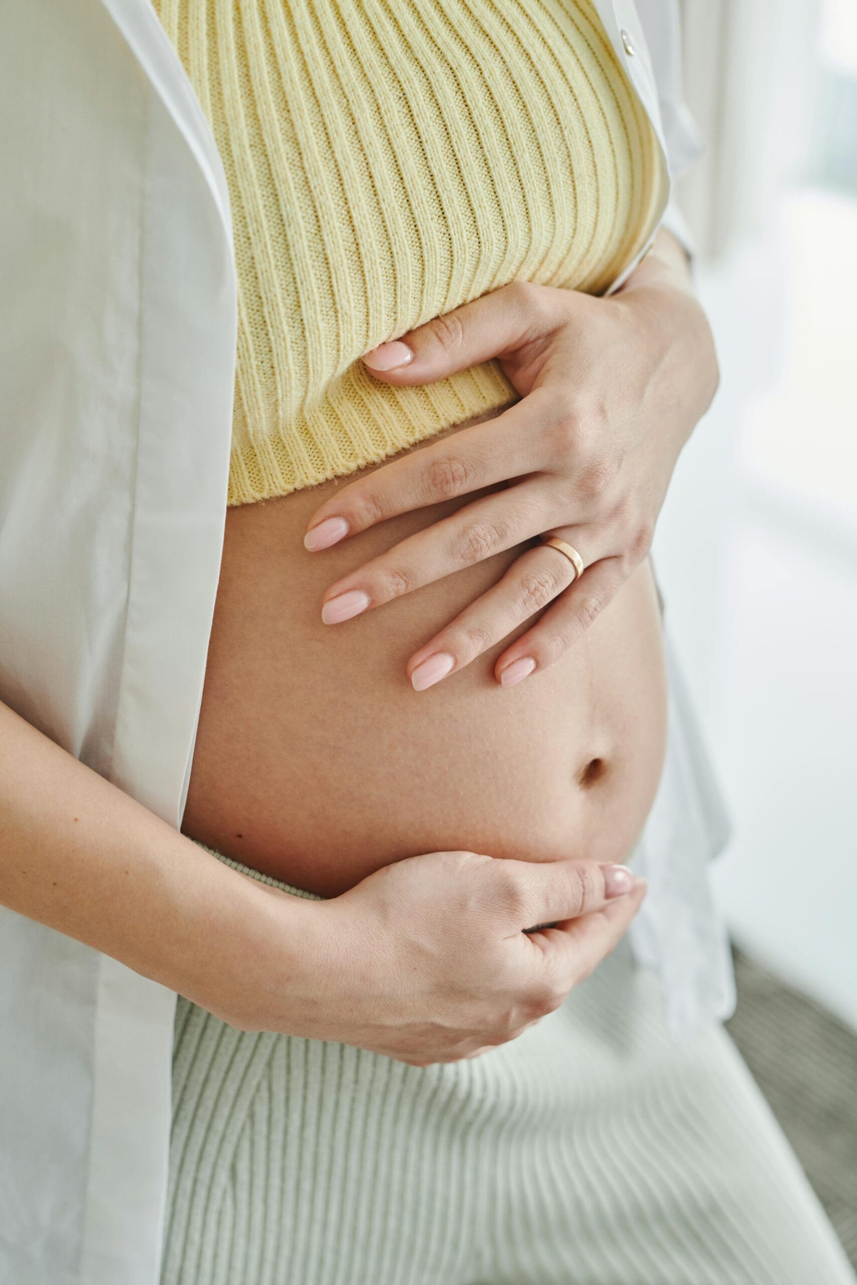 Pregnant woman wearing a yellow shirt with her pregnant belly out.