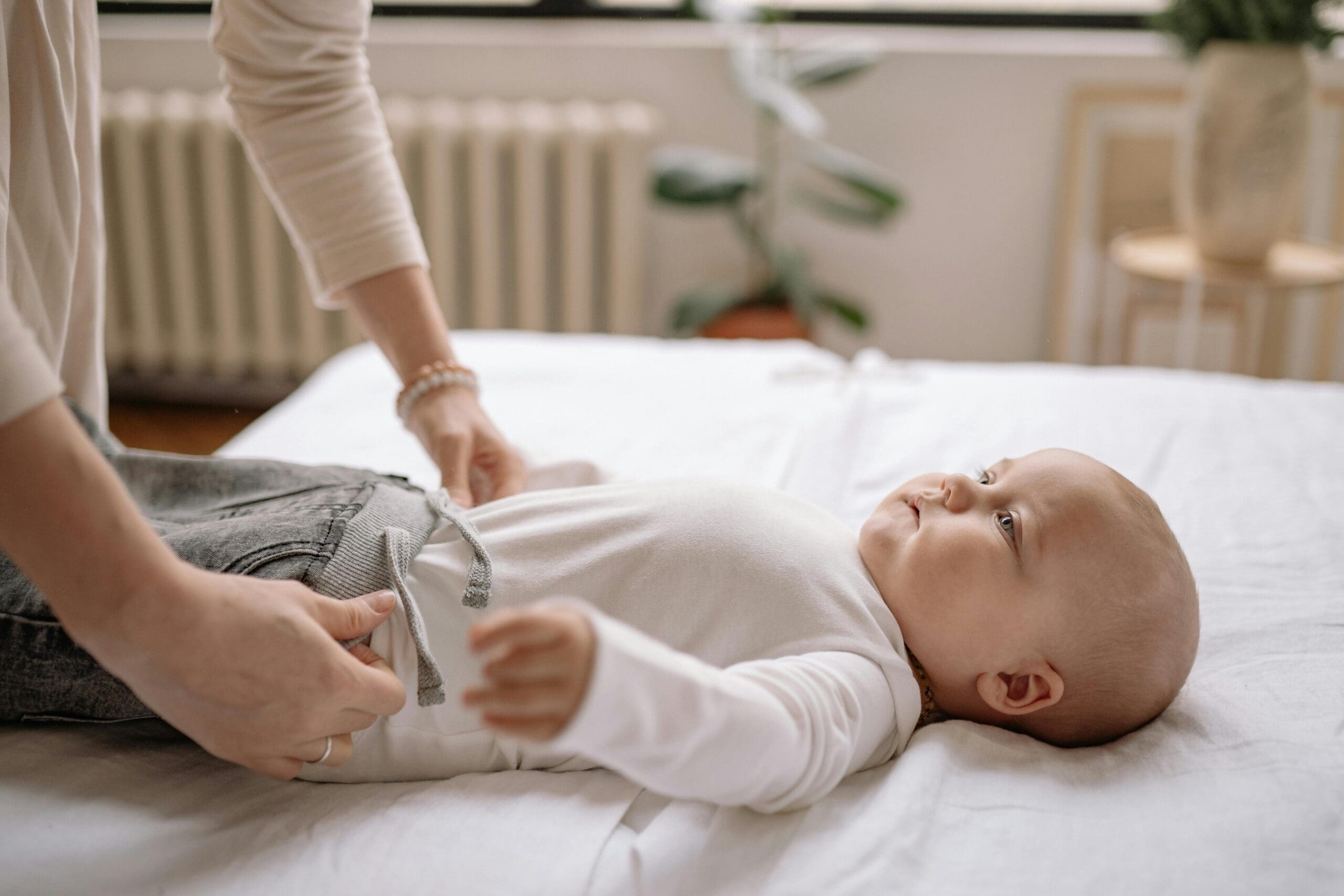 Baby laying on a table with a white table wearing white sweatpants and a white shirt.